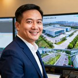 深圳龙岗科技园物业经理李总的半身照片，他穿着深蓝色西装，面带微笑站在园区监控中心大屏前
